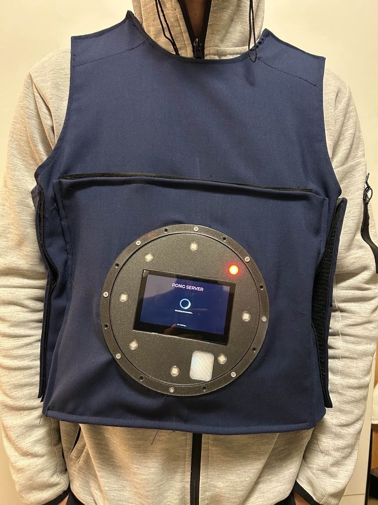 Getragene Weste mit rundem Modul, auf dem Display läuft der Startbildschirm